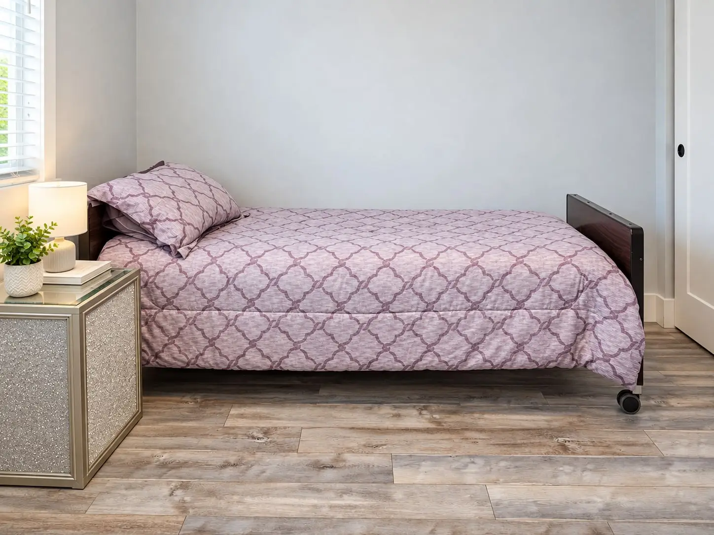 Bed with a pink quilt beside a nightstand and small plant